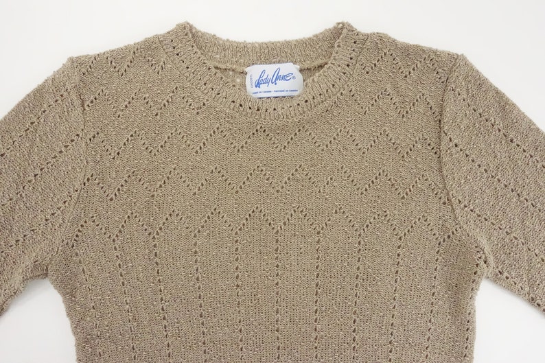 May include: A beige knitted sweater with a delicate openwork pattern. The sweater has a round neckline and long sleeves. The label reads "Lady Grace".