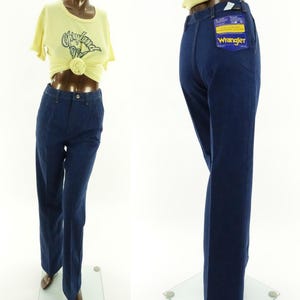 May include: A pair of dark blue denim jeans with a wide leg. The jeans have a Wrangler tag on the back pocket.