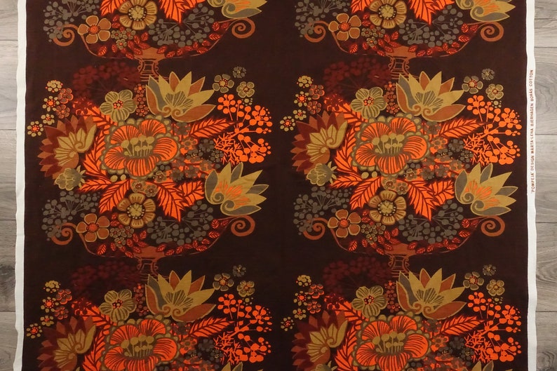 May include: A brown fabric with a repeating pattern of orange, brown, and green flowers in a vase. The fabric has a vintage feel.