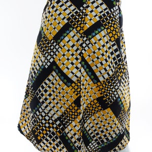 May include: A black, white, and yellow patterned skirt with a geometric design. The skirt has a slight A-line shape and a curved hem.