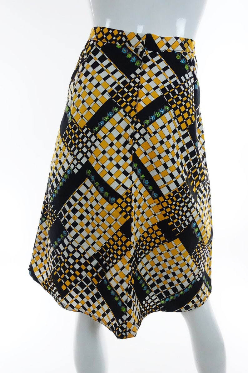 May include: A black, white, and yellow patterned skirt with a geometric design. The skirt has a slight A-line shape and a curved hem.