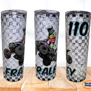 May include: A white and black checkered tumbler with a photo of a person riding an ATV. The tumbler has the name "FRALEY" and the number "110" printed on it.