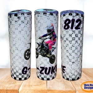 May include: A white stainless steel tumbler with a checkered pattern and a motocross rider graphic. The tumbler has a black lid and a purple inscription that reads "G-ZUK" and "812".