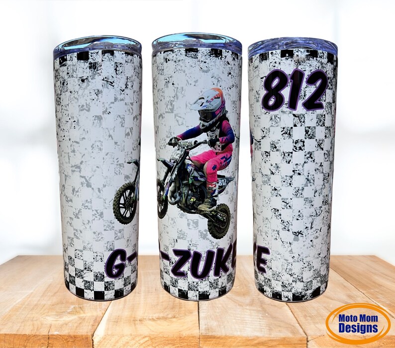May include: A white stainless steel tumbler with a checkered pattern and a motocross rider graphic. The tumbler has a black lid and a purple inscription that reads "G-ZUK" and "812".