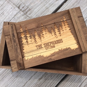 May include: A wooden box with a hinged lid. The lid is engraved with a forest scene and the text "THE SHEPHARDS EST. 2016".