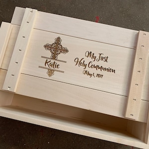 May include: A wooden box with a hinged lid, engraved with a cross, the name "Katie", and the text "My First Holy Communion May 6, 2017".