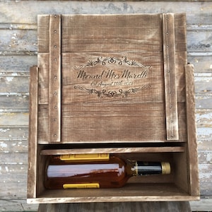May include: A wooden box with a hinged lid and a pull-out drawer. The box is engraved with the text "Mr. and Mrs. Mardelli Est. August 18th, 2018". A bottle of liquor is inside the drawer.