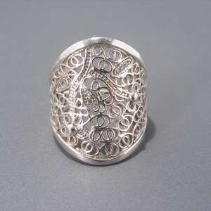 May include: A silver filigree ring with a delicate, intricate design. The ring is wide and has a rounded shape.