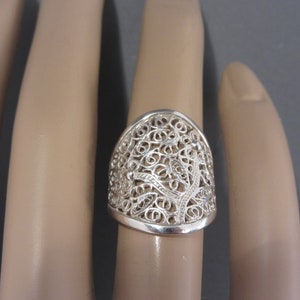 May include: A silver filigree ring with a delicate, intricate design. The ring is wide and has a rounded top.
