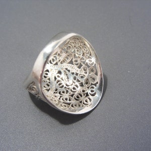 May include: A silver filigree ring with a delicate, intricate design. The ring is open and has a wide band.