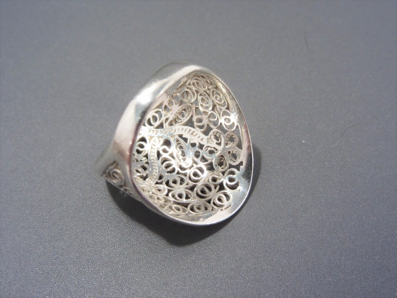 May include: A silver filigree ring with a delicate, intricate design. The ring is open and has a wide band.