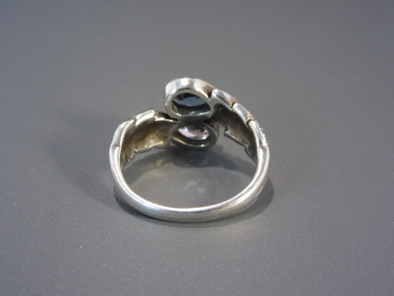 May include: A silver ring with two blue and purple stones set in a twisted band.