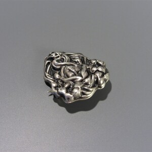 Pode incluir: Um broche de prata com um design floral. O broche &eacute; feito de uma &uacute;nica pe&ccedil;a de metal e tem uma superf&iacute;cie texturizada.
