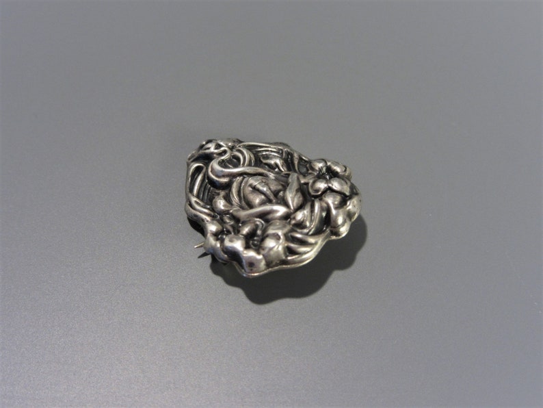 Pode incluir: Um broche de prata com um design floral. O broche &eacute; feito de uma &uacute;nica pe&ccedil;a de metal e tem uma superf&iacute;cie texturizada.