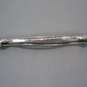 May include: A silver filigree brooch with a delicate design. The brooch has a pin and catch closure.