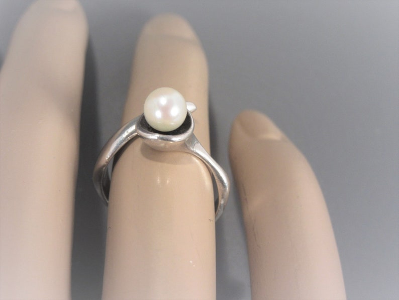 Puede incluir: Un anillo de plata con una perla blanca engastada en un dise&ntilde;o abstracto &uacute;nico.