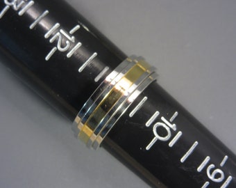 May include: A silver and gold ring with multiple bands. The ring is on a black ruler.