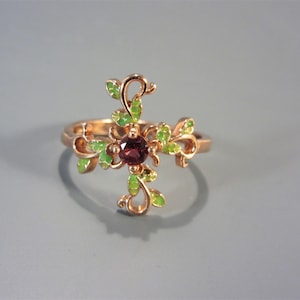 May include: A gold ring with a red gemstone in the center and green enamel leaves surrounding it.