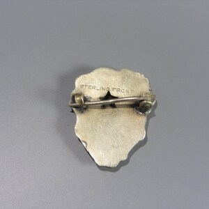 Pode incluir: Pin de tom prateado com um design detalhado. A parte de tr&aacute;s do pin tem as palavras "STERLING FRONT" gravadas.