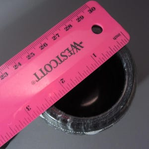 Pu&ograve; includere: Un mortaio maculato bianco e nero con un righello rosa sopra. Il righello &egrave; contrassegnato in pollici e presenta il logo Westcott. Il mortaio ha un diametro di circa 7,6 cm.