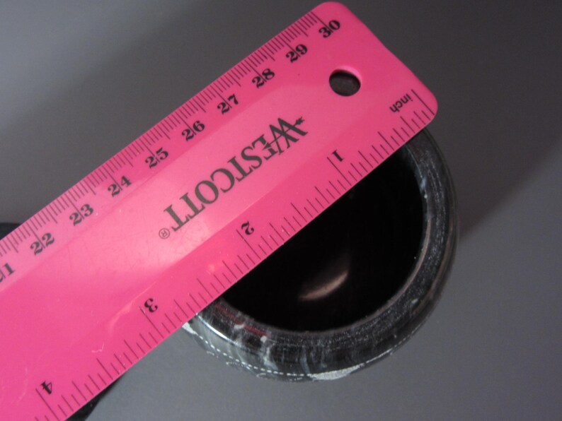 Pu&ograve; includere: Un mortaio maculato bianco e nero con un righello rosa sopra. Il righello &egrave; contrassegnato in pollici e presenta il logo Westcott. Il mortaio ha un diametro di circa 7,6 cm.