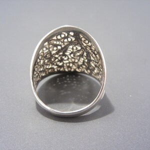 May include: A silver filigree ring with a delicate, intricate design. The ring is wide and has a rounded top.