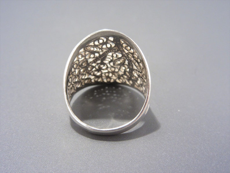May include: A silver filigree ring with a delicate, intricate design. The ring is wide and has a rounded top.