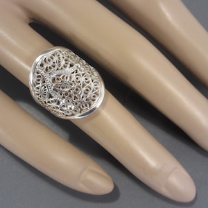 May include: A silver filigree ring with an oval design. The ring is intricate and delicate, with a floral pattern.