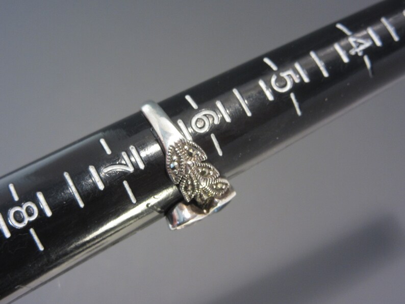 May include: A silver ring featuring a blue stone and a floral design set with marcasite stones.