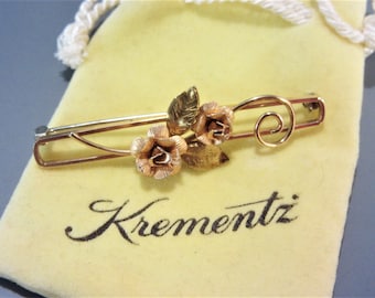 Peut inclure: Une broche dorée avec deux fleurs en forme de rose et des feuilles. La broche est sur un sac en velours jaune avec le mot "Krementz" imprimé dessus.