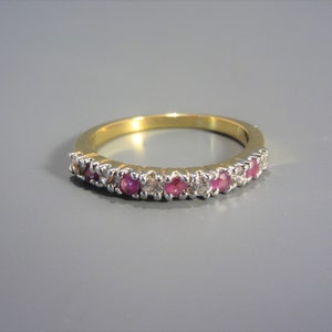 May include: A gold band ring with a row of alternating pink and white gemstones.