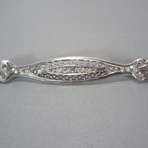 May include: A silver filigree brooch with a row of clear rhinestones in the center.