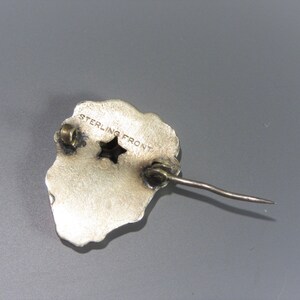 Pode incluir: Broche prateada com um design em forma de estrela e as palavras "STERLING FRONT" gravadas no verso.