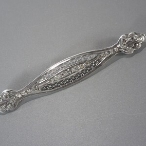 May include: A silver brooch with a delicate filigree design and clear rhinestones.
