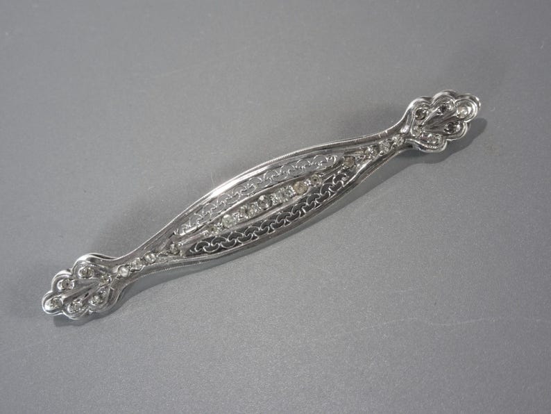 May include: A silver brooch with a delicate filigree design and clear rhinestones.