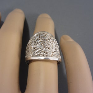 May include: A silver filigree ring with a delicate, intricate design. The ring is wide and has a rounded top.