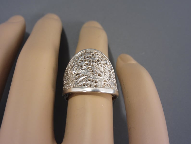 May include: A silver filigree ring with a delicate, intricate design. The ring is wide and has a rounded top.