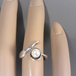 Puede incluir: Un anillo de plata con una perla blanca engastada en una banda curva.