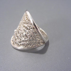 May include: A silver filigree ring with a triangular shape. The ring is made of delicate, intricate wirework.