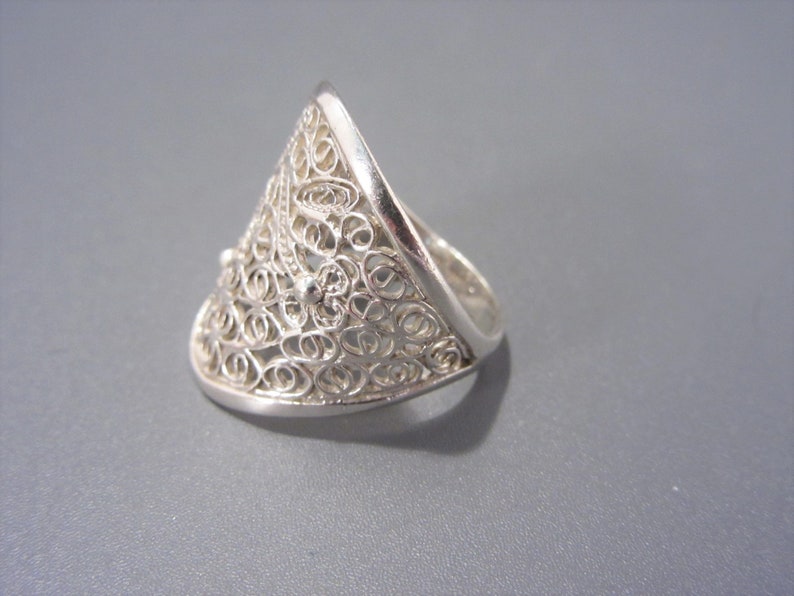 May include: A silver filigree ring with a triangular shape. The ring is made of delicate, intricate wirework.