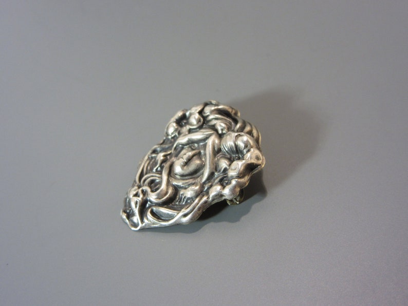 Pode incluir: Um broche de prata com um design detalhado de um rosto de mulher rodeado de flores.