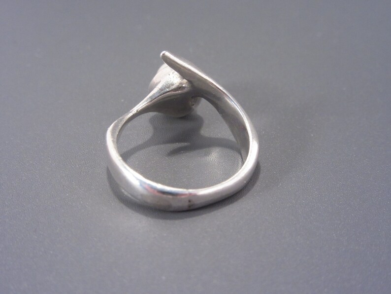 Puede incluir: Un anillo de plata con un dise&ntilde;o abstracto &uacute;nico. El anillo est&aacute; hecho de metal liso y pulido y tiene un estilo simple y moderno.
