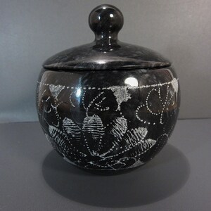 Pu&ograve; includere: Un vaso di marmo nero con coperchio. Il vaso rotondo presenta un motivo floreale bianco. Il coperchio ha una piccola maniglia rotonda. Questo vaso &egrave; probabilmente per la conservazione o l'esposizione.