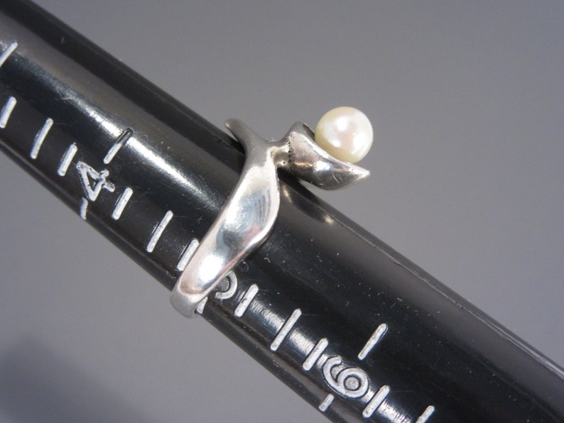 Puede incluir: Un anillo de plata con una perla engastada en un dise&ntilde;o curvo.