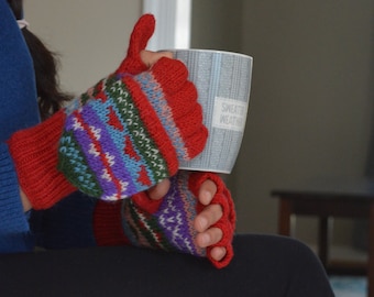 May include: Red and patterned knit fingerless gloves and leg warmers. The gloves have a red base with colourful geometric patterns in blue, green, purple, and white. A mug with the text "Sweater Weather" is held in the gloves.
