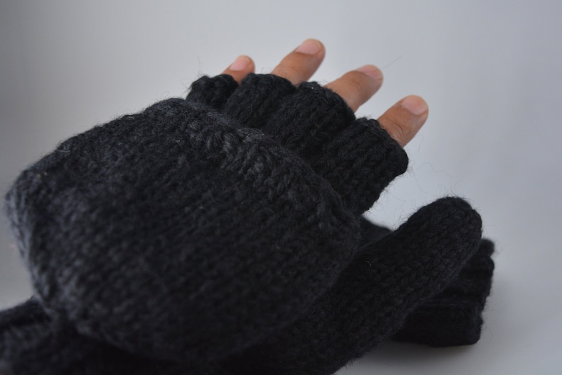 May include: A pair of dark gray fingerless gloves, knitted with a textured yarn. The gloves have open fingertips and a wrist cuff. The image shows the gloves on a hand against a light gray background. The gloves appear to be warm and suitable for cold weather.