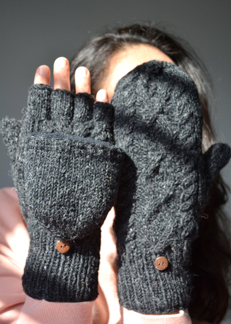 May include: Dark gray knitted convertible mittens with a button closure. The mittens have a textured pattern and can be worn as fingerless gloves or mittens. The buttons are brown.