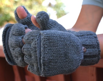 May include: Gray knitted convertible mittens with a button closure. The mittens have a flap that can be folded back to expose the fingers, transforming them into fingerless gloves. The knitted texture is visible, and the mittens appear warm and cozy.