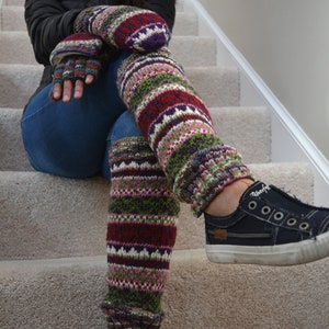 May include: A pair of colorful knitted leg warmers with a striped pattern in shades of red, green, pink, and white. The leg warmers are worn with blue jeans and black sneakers.