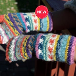 May include: A pair of colorful knitted fingerless gloves. The gloves feature a vibrant mix of colors including orange, yellow, blue, purple, and white. The design includes geometric patterns and heart shapes. A red circle with the word "NEW" is visible.